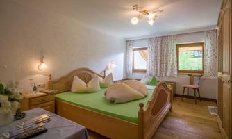 A cozy bedroom with a large wooden bed and colorful pillows. The room has plenty of natural light and a friendly atmosphere.