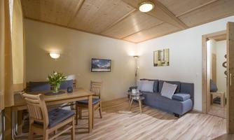 A cozy living room with a wooden ceiling and modern furniture. There is a dining table, a couch, and a bright atmosphere.