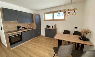 A modern kitchen with wood and gray tones. There are four chairs at the table and a cozy atmosphere is present.