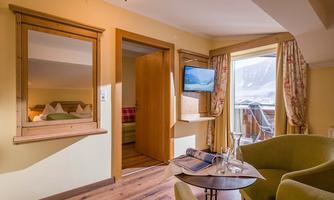 A cozy hotel room with a green armchair and a small table. Through the window, you can see a beautiful view of the mountains.