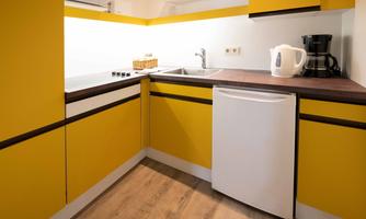 A modern kitchen with yellow cabinets and a wooden countertop. It is equipped with a sink, fridge, and coffee machine.