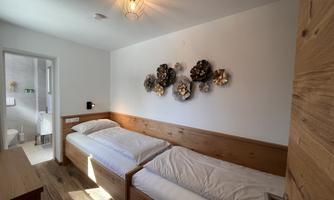 A cozy bedroom with two wooden single beds.  
Decorative wall pictures hang on the wall, and there is plenty of natural light.