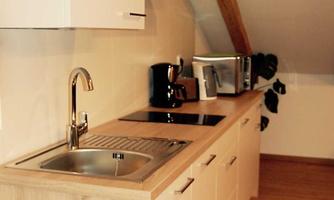 A modern kitchen unit in an attic with wooden shelves. The kitchen has a sink, stove, and modern appliances.