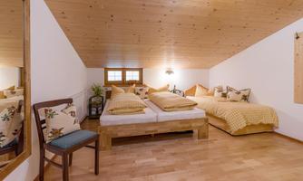 A bright room with a wooden ceiling and two beds. There is a chair and decorative cushions for a cozy design.