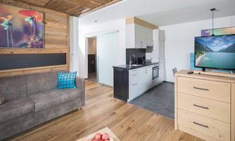 A modern kitchen with a cozy seating area and a wooden table. The room has large windows and is decorated in bright colors.