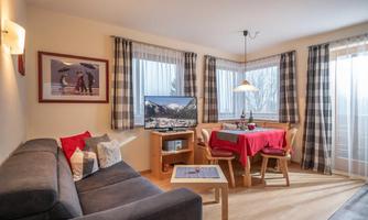 A cozy living room corner with a sofa and a dining table. Large windows let in plenty of light, and the room is tastefully furnished.