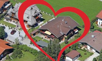 Aerial view of several residential buildings in a green environment. In the center is a large red heart that frames the houses.
