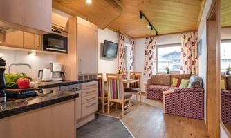 A modern kitchenette with wooden elements and a dining area. The living space is cozily furnished with a sofa and large windows.