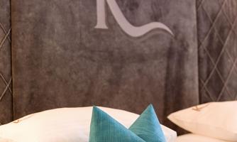 An elegant hotel room with a large, soft bed and a stylish headboard wall. Cushions in various sizes create a cozy atmosphere.