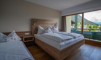 A cozy bedroom with two beds and modern wooden furniture. A mountain landscape can be seen through the window.