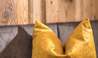 A cozy pillow in bright yellow on a dark bench. The background consists of warm wooden panels.