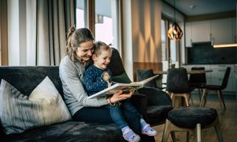 A mother is reading with her smiling child in a modern living room. The cozy atmosphere is enhanced by the soft lighting and stylish furnishings.