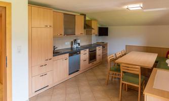 A modern kitchen with wooden cabinets and modern appliances. A dining table with chairs completes the space.