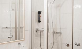 A modern bathroom with a shower and a sink. The walls are covered in light tiles and there is a large mirror.