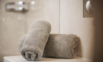 Two gray towels are neatly rolled up on a bathroom shelf. In the background, tiles and bathroom fixtures are visible.