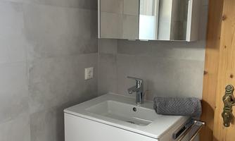 A modern bathroom with a white vanity combination and a mirror. The walls are designed in neutral gray tones.