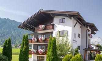 A charming building with balconies and colorful flowers hangs in the greenery. The mountains are visible in the background.