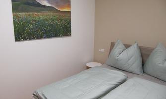 A cozy bedroom with a double bed and cushions in fresh shades of green. A beautiful picture of a blooming landscape at sunset hangs on the wall.
