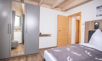 A modern bedroom with a bed, a mirrored wardrobe, and warm wooden elements. The walls are kept in light colors, creating an inviting impression.