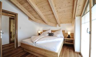 A cozy bedroom with wooden beds and slanted ceilings. Large windows let in plenty of daylight and create an inviting atmosphere.