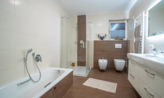 A modern bathroom with a bathtub, a shower, and a stylish sink. The walls are light and the floor has a wood look.
