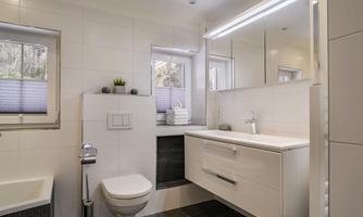 A modern bathroom with white tiles and an elegant washbasin. The window lets natural light in.