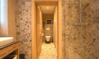 A modern bathroom with natural stone walls and a shower. On the right is a toilet, and on the left is a sink with wooden details.