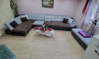 A cozy living room with a large U-shaped sofa and bright walls. A table with decorations and plants adds an inviting atmosphere to the space.