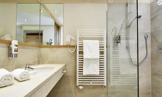 A modern bathroom with a glass shower and bright tiles. Clean towels are on the shelf, and the room has large mirrors.