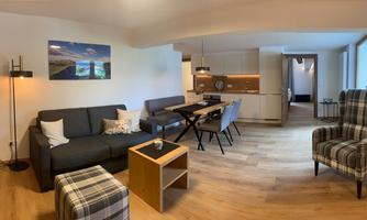 A modern living room with a comfortable couch, a dining table, and stylish chairs. Large windows provide plenty of daylight.