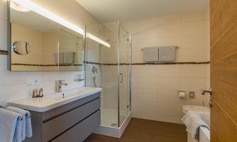 A modern bathroom with a shower and a sink. The walls are light and the floor has a dark wood tone.