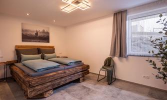 A modern bedroom with a large wooden bed and cool colors. The room has plenty of daylight and a cozy atmosphere.