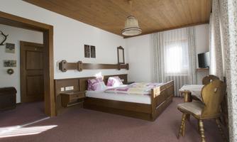 A bright bedroom with a double bed and wood paneling. The room is cozily furnished and has a small table with chairs.
