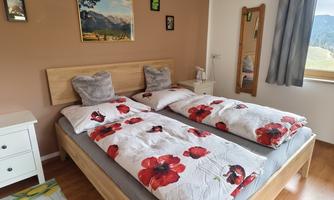 A cozy bedroom with two single beds and colorful bed covers. Pictures hang on the wall, and a window offers a view outside.