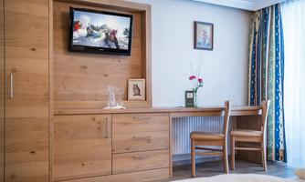 A cozy room with wooden furniture and a television on the wall. A table with two chairs and a flower vase creates an inviting atmosphere.