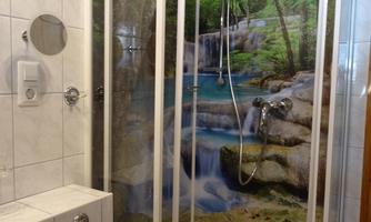 A modern shower with a glass cabin design and a nature wallpaper in the background. The room feels bright and inviting.