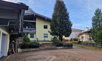 A quiet courtyard with a yellow house and trees. The paved area is well-maintained and invites you to linger.