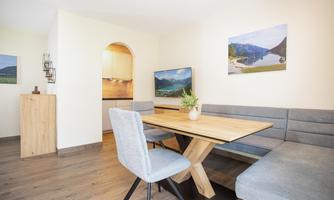 A bright dining room with a wooden table and comfortable benches. Pictures of mountain landscapes hang on the walls.