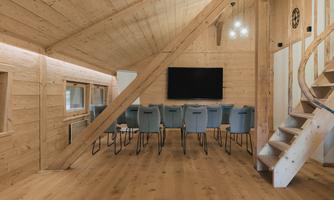A modern meeting room with wooden paneling and a long row of tables. There is a large television on the wall, and a staircase leads to the upper floor.