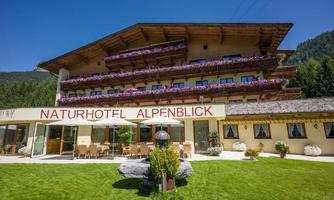 A beautiful nature hotel with flowering balconies and a well-kept garden. The surroundings are enclosed by mountains and trees.