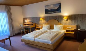 A cozy hotel room with two beds, wooden furniture, and soft lighting. A desk and a window with curtains complete the space.