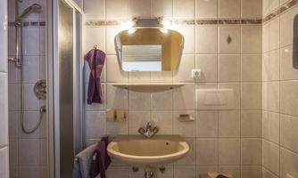 A small bathroom with a shower and a sink. The walls are tiled and decorated with purple towels.