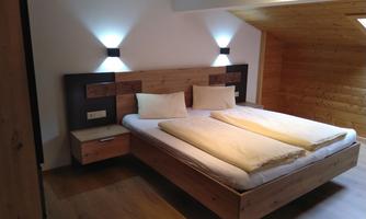 A cozy bedroom with a wooden double bed. The walls are bright and the lighting creates a pleasant atmosphere.
