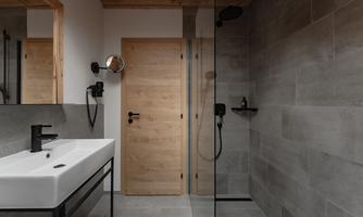 A modern bathroom with an elegant shower and a minimalist sink. The walls are tiled in gray, and the wooden decor creates a warm atmosphere.