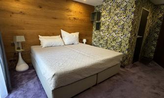 A modern bedroom with a double bed and a floral wallpaper. The room has a cozy rug and a stylish bedside lamp.