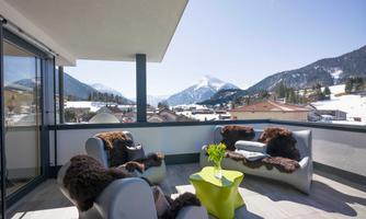 A modern terrace with comfortable seating and a view of the mountains. The sky is clear and the surroundings are covered in snow.