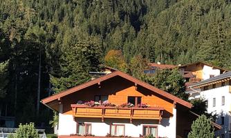 A charming house with a red roof, surrounded by trees. In the background, green mountains can be seen.