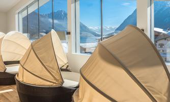 A bright room with comfortable loungers and large windows. Outside, mountains and a clear sky can be seen.