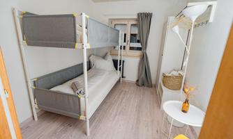 A simple bedroom with a bunk bed and a single bed. There is a small table and a basket for decoration.