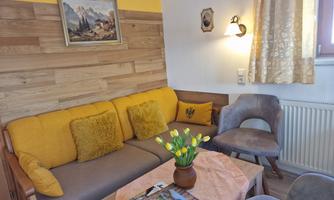 A cozy living space with a yellow couch and a wooden wall setup. Fresh tulips and some magazines are on the table.